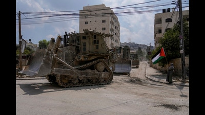 A man waves the Palestinian flag as a convoy of Israeli military bulldozers drive by during an army raid in Jenin, West Bank, Monday, Sept. 2, 2024. (AP Photo/Majdi Mohammed) (AP) A man waves the Palestinian flag as a convoy of Israeli military bulldozers drive by during an army raid in Jenin, West Bank, Monday, Sept. 2, 2024. (AP Photo/Majdi Mohammed) (AP)