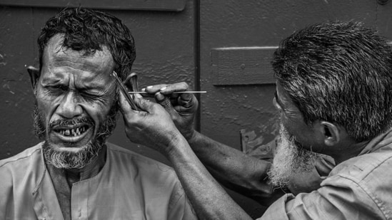 An itinerant 'kaan-saaf-wallah (ear-cleaner), armed with his strange array of tools, attending to a customer on the roadside at Kumortuli, Kolkata.&nbsp;(Photo by Sandipan Mukherjee)