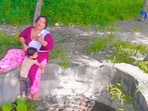 The image shows a kid clutching onto a woman’s leg who is sitting on the edge of an open well. 