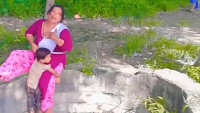 The image shows a kid clutching onto a woman’s leg who is sitting on the edge of an open well. (Screengrab) The image shows a kid clutching onto a woman’s leg who is sitting on the edge of an open well. (Screengrab)