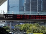 People walk on an overpass with a display of stock information in front of buildings in the Lujiazui financial district in Shanghai, China.