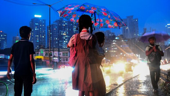 Two school students share an umbrella to shield themselves during rain, in Mumbai, (PTI)