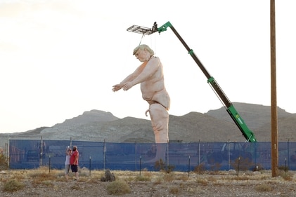 Las Vegas resident Christine Richardson takes a photo with husband Marc outside a fenced-in lot displaying a 43-foot-tall (13 meters) naked statue resembling former US President and Republican presidential candidate Donald Trump, near Interstate 15 north of Las Vegas, Nevada, September 28, 2024. Made of foam over rebar and weighing approximately 6,000 pounds (2722 kilos), the gigantic display will will criss-cross the US as part of the "Crooked and Obscene Tour." (Photo by Ronda Churchill / AFP) (AFP)