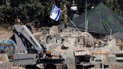An Israeli member of the military adjusts an Israeli flag as armoured vehicles are arranged in formation, amid cross-border hostilities between Hezbollah and Israel, in northern Israel, September 30, 2024. REUTERS/Jim Urquhart