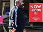 A pedestrian walks past a "Now Hiring" sign posted on a business storefront in San Gabriel, California. August saw job openings increase to 8.04 million, led by construction, amid a declining hiring rate. The labor market remains mixed, prompting potential interest rate adjustments by the Federal Reserve.