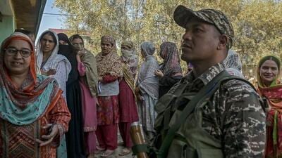 Security personnel stands guard as voters queue up to cast their ballots at a polling station in Bandipora during the third and final phase of voting for the Jammu and Kashmir Assembly elections on October 1. (AFP)