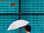A woman walks in front of an electronic quotation board displaying stock prices of Nikkei 225 on the Tokyo Stock Exchange in Tokyo.