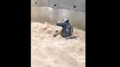 The biker, caught off guard by the sudden rise in water levels, loses balance and is thrown off his bike as the water rapidly rushes through the passage. (X) The biker, caught off guard by the sudden rise in water levels, loses balance and is thrown off his bike as the water rapidly rushes through the passage. (X)