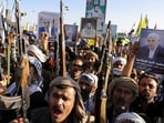 People hold firearms and posters of the late Hamas leader Yahya Sinwar during a rally by protesters, mainly Houthi supporters.