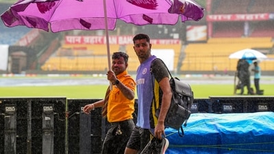 A security guard holds an umbrella to cover cricketer Harshit Rana as it rains at the M Chinnaswamy Stadium, ahead of the first test match between India and New Zealand (PTI) A security guard holds an umbrella to cover cricketer Harshit Rana as it rains at the M Chinnaswamy Stadium, ahead of the first test match between India and New Zealand (PTI)