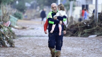 A Civil Protection member carries a child in a street covered in mud in a flooded area in Picanya. (AFP) A Civil Protection member carries a child in a street covered in mud in a flooded area in Picanya. (AFP)