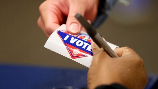 A poll worker hands a voter an "I Voted" sticker at a polling location inside Henderson Executive Airport during the last day of early voting in Henderson, Nevada, US, on Friday, Nov. 1, 2024. Donald Trump and his allies are telling supporters that they're on pace for a runaway victory barring fraud, setting the stage for outrage and legal challenges if the election doesn't break in favor of Republicans. Photographer: Ian Maule/Bloomberg (Bloomberg)