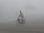 A man wears a mask to avoid smog while he rides on a bicycle along a road in Multan