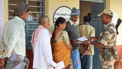 Channapatna: A security personnel checks voter ID as voters wait to cast votes at a polling station during the Channapatna Assembly by-poll, Karnataka. (PTI) Channapatna: A security personnel checks voter ID as voters wait to cast votes at a polling station during the Channapatna Assembly by-poll, Karnataka. (PTI)