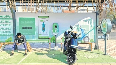 A man checks his mobile phone as he waits while recharging his Ola electric scooter at an electric vehicle charging station in New Delhi. (REUTERS)