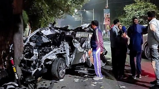 People gather around the car that got mangled after it hit a container, in Dehradun on Monday. (ANI)