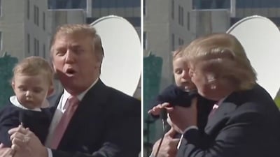 In the clip, shared on X, Donald Trump is seen holding baby Barron in his arms as he stands in front of a podium. (X/@DefiantWorld) In the clip, shared on X, Donald Trump is seen holding baby Barron in his arms as he stands in front of a podium. (X/@DefiantWorld)
