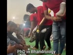 In the video, posted on X, four men serve cutlery to a long row of people sitting on the floor, waiting to be served food.