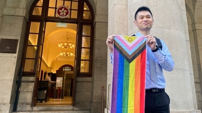 Nick Infinger, who won a years-long legal battle over the differential treatment facing same-sex couples, holds up a rainbow banner after speaking to media members outside Hong Kong’s top court on Tuesday, Nov. 26, 2024. (AP)
