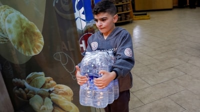 A boy carries water bottles to the car on his way back to southern Lebanon, in Sidon. (REUTERS)