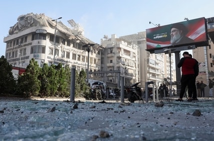 A billboard depicting late Hezbollah leader Sayyed Hassan Nasrallah is pictured as people stand near a damaged building, in the aftermath of an Israeli strike in the Chiyah district of Beirut's southern suburbs. (REUTERS)