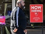 A pedestrian walks past a "Now Hiring" sign posted on a business storefront in San Gabriel, California