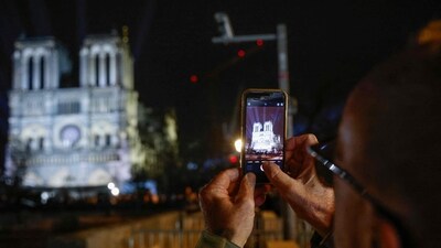 A man takes a photograph of Notre Dame de Paris cathedral on the eve of its official reopening after more than five years of reconstruction work following the April 2019 fire, in Paris on December 6, 2024. Notre-Dame Cathedral is set to re-open in early December 2024,&nbsp; (AFP)