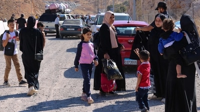 People fleeing Israeli bombardment in Lebanon, carry their belongings as they prepare to continue their journey on foot along a road damaged by an Israeli strike, in the area of Masnaa on the Lebanese side of the border crossing with Syria 