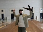 A man holds an AK-47 and flashes the victory sign as he poses for a photo in a hall of Syrian President Bashar Assad's presidential palace in Damascus, Syria, Sunday, Dec. 8, 2024.