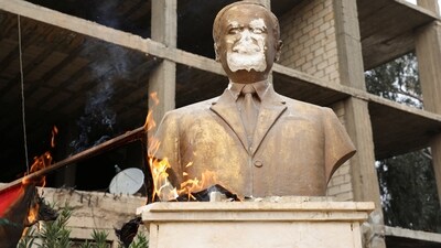 Flames rise near a damaged statue of former Syrian president Hafez al-Assad, after rebels seized the capital and ousted President Bashar al-Assad, in Qamishli. (REUTERS)