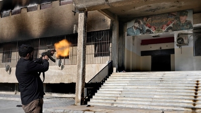 A Syrian fighter from rebel group, fires towards a poster at the entrance of the notorious security detention centre called Palestine Branch, which pictures the late Syrian President Hafez Assad and his son the ouster Syrian president Bashar Assad, in Damascus, Syria, Saturday, Dec. 14, 2024. (AP) A Syrian fighter from rebel group, fires towards a poster at the entrance of the notorious security detention centre called Palestine Branch, which pictures the late Syrian President Hafez Assad and his son the ouster Syrian president Bashar Assad, in Damascus, Syria, Saturday, Dec. 14, 2024. (AP)