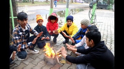 Children sit around the bonfire to keep themselves warm on a cold winter day in Rohtak on Sunday. (Manoj Dhaka/HT)