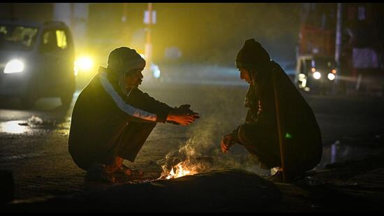 Two people sit around a bonfire to stave off the cold. (Sanchit Khanna/HT Photo)