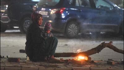 A woman and her child warm themselves by a fire on a cold winter evening in Gurugram on Monday. (Parveen Kumar/Hindustan Times)