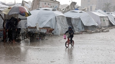 A Palestinian child rides his bicycle past drenched tents during a rain storm at a makeshift camp in Gaza City on December 31, 2024. (AFP/Omar Al-Qattaa)