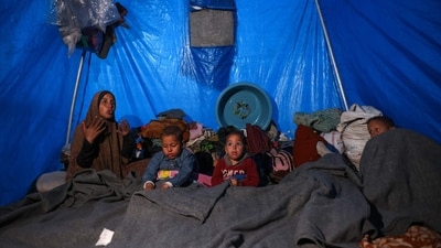 A woman sits next to her children inside a shelter at a camp for displaced Palestinians in Khan Yunis, in the southern Gaza Strip on December 29, 2024. (AFP/Basher Taleb)