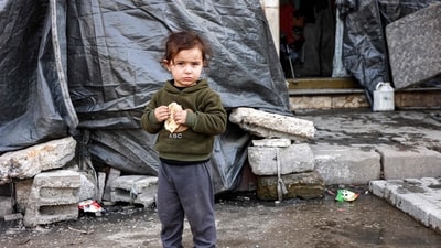 A child holds a half-eaten piece of bread while standing outside a tent at a shelter for displaced Palestinians in Gaza City on December 11, 2024. (AFP/Omar Al-Qattaa)