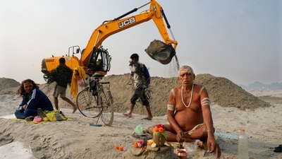 A Sadhu prays sitting next to an earthmover moving sand on the banks of the Ganga, ahead of Maha Kumbh Mela in Prayagraj. (AP)