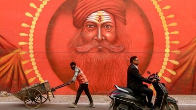 A worker pushes a wheelbarrow carrying trash, past a wall mural ahead of the Maha Kumbh Mela in Prayagraj. (AFP)