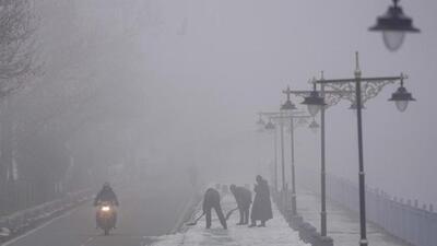Workers clearing snow from a pavement on a cold and foggy morning on the outskirts of Srinagar on Friday. (AP Photo)