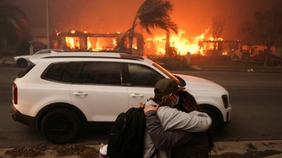 People embrace as they evacuate following powerful winds fueling devastating wildfires in the Los Angeles area, at the Eaton Fire in Altadena, California, (REUTERS)