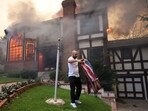 A person folds a flag after lowering it from the flagpole outside his burning cousin's house as powerful winds fueling devastating wildfires in the Los Angeles area force people to evacuate, at the Eaton Fire in Altadena, California,