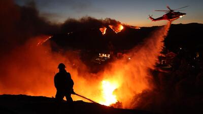 Fire personnel try to control the blaze on ground while a helicopter drops water as the wildfire grows in Pacific Palisades, California on January 7. (AFP Photo) Fire personnel try to control the blaze on ground while a helicopter drops water as the wildfire grows in Pacific Palisades, California on January 7. (AFP Photo)