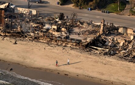 In this aerial view taken from a helicopter, a man waves on the beach in front of burned homes during the Palisades fire in the Malibu, Los Angeles county, (AFP)