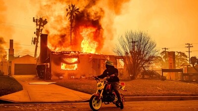 A motorcyclist stops to look at a burning home during the Eaton fire in the Altadena area of Los Angeles county. (AFP)