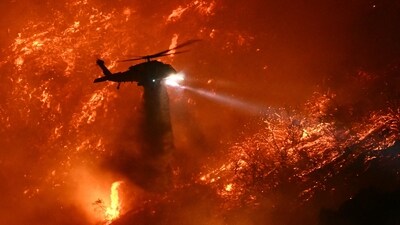 A fire fighting helicopter drops water as the Palisades fire grows near the Mandeville Canyon neighborhood and Encino, California, on January 11, 2025. (AFP)