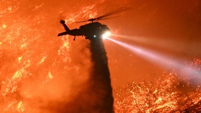 A fire fighting helicopter drops water as the Palisades fire grows near the Mandeville Canyon neighborhood and Encino. (AFP) A fire fighting helicopter drops water as the Palisades fire grows near the Mandeville Canyon neighborhood and Encino. (AFP)
