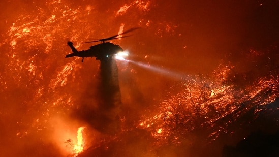 A fire fighting helicopter drops water as the Palisades fire grows near the Mandeville Canyon neighborhood and Encino, California, on January 11, 2025. (AFP)