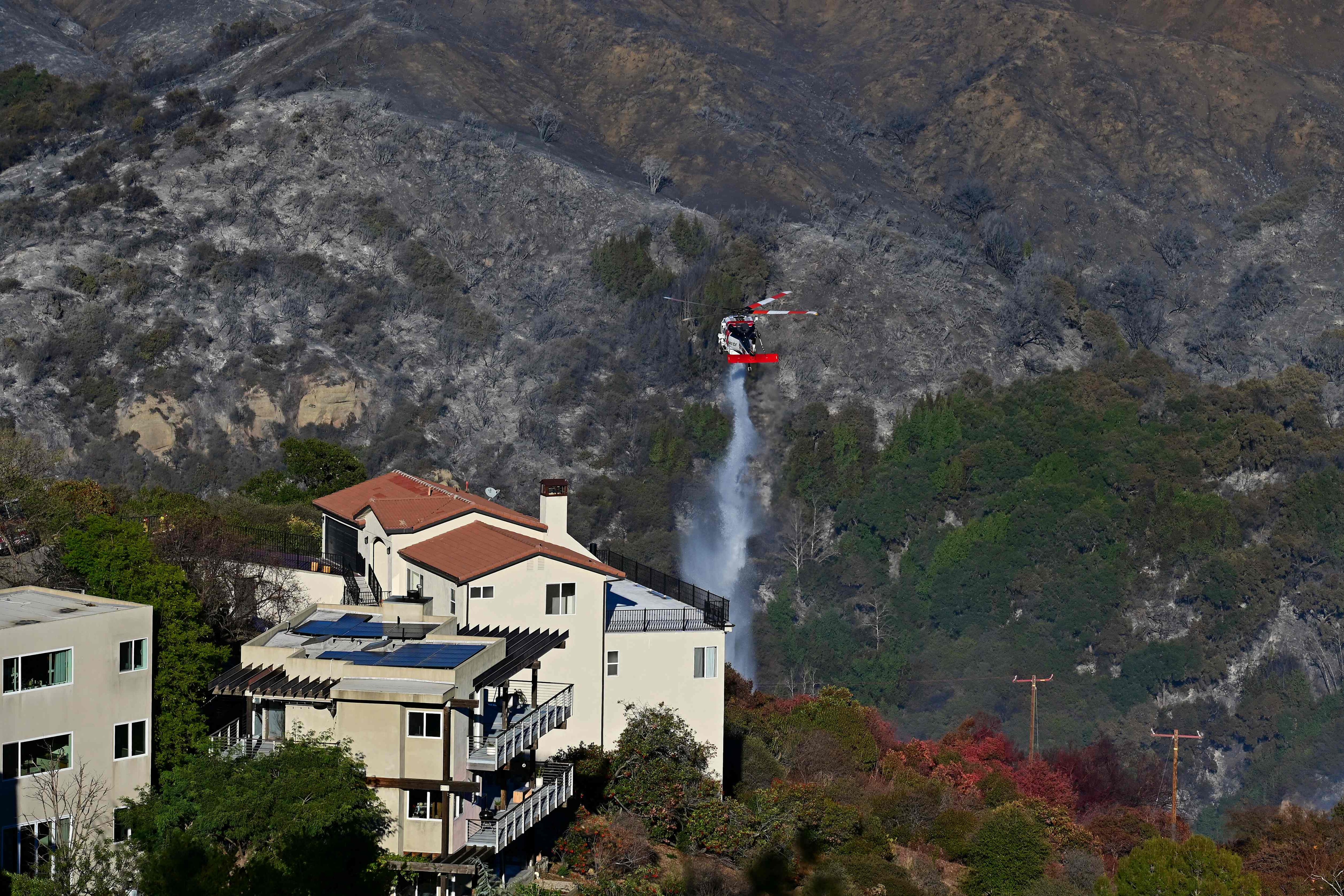 A CalFire helicopter drops water next to a building near hillsides scorched by the Palisades Fire in Fernwood, Topanga, a community in western Los Angeles County, California. (AFP) A CalFire helicopter drops water next to a building near hillsides scorched by the Palisades Fire in Fernwood, Topanga, a community in western Los Angeles County, California. (AFP)