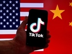 TikTok logo is displayed on the screen of an iPhone in front of a US flag and Chinese flag background in Washington, DC.